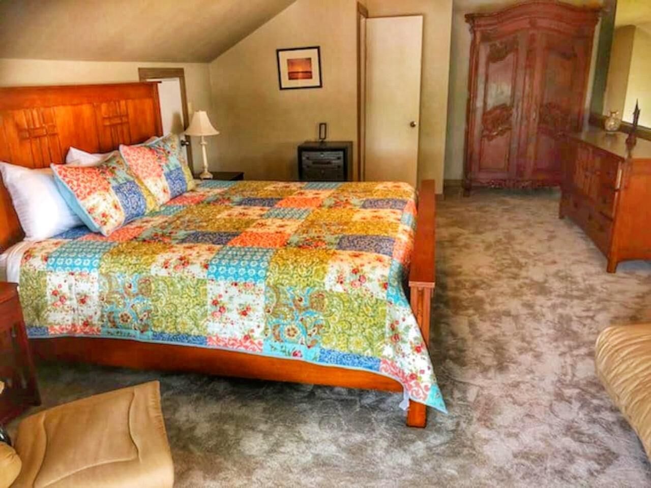 Un dormitorio con cama de madera, colcha, mesita de noche, cómoda y piso alfombrado.