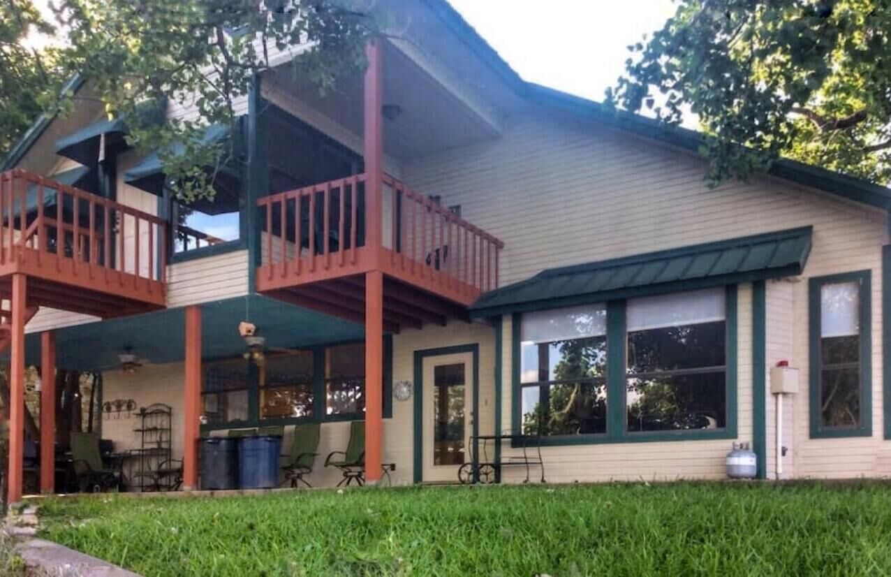 A two-story house with a balcony, a porch with chairs, and a gas tank in the yard.