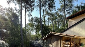 Une terrasse en bois avec une table ronde et des chaises, entourée d’arbres et d’un petit bâtiment doté d’un toit en pente.