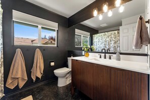 A modern bathroom with a dark wall, wooden vanity, white sink, and a large mirror. - West Nine Stunning Views & Hot Tub (Port Angeles)