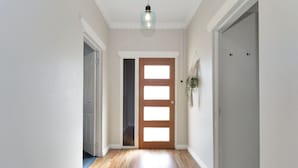 A hallway with wooden flooring, a wooden door with a glass panel, and a hanging light fixture. - North Central Vacation Home (North Mackay)