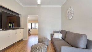 A modern living room with a grey sofa, striped ottomans, and a flat-screen TV on a cabinet. - North Central Vacation Home (North Mackay)