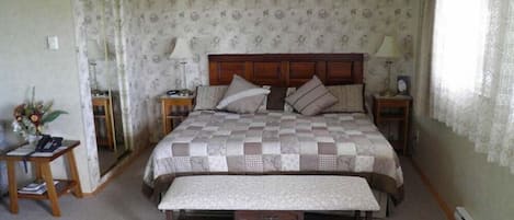 Un dormitorio con una cama grande, dos mesitas de noche, un banco y papel tapiz floral.