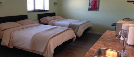 A room with two beds, a window, a painting of a red telephone booth, and a kitchenette with a sink and coffee maker.