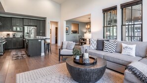 A spacious living area with a grey sofa, a coffee table, and a kitchen area with dark wood cabinets and modern appliances.