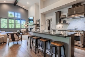 A spacious kitchen with a large island, bar stools, and a dining area with a sofa and chairs. - Modern Creekside Townhome with Private Hot Tub! Fireplace! (Mammoth Lakes)