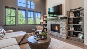 A modern living room with a fireplace, large windows, a sofa, and a coffee table.
