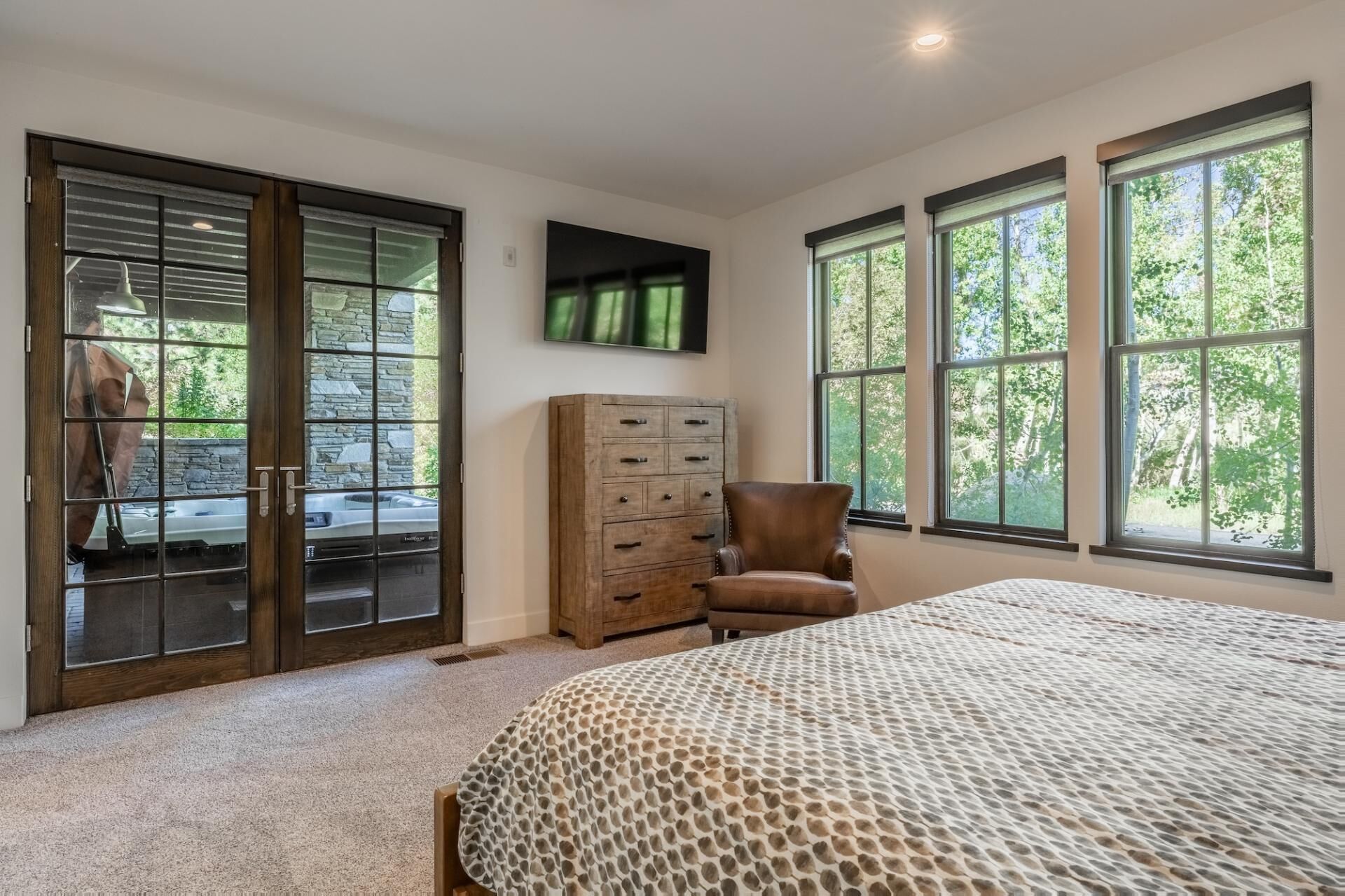 Une chambre à coucher avec un grand lit, une commode en bois, un fauteuil en cuir et un téléviseur fixé au mur.
