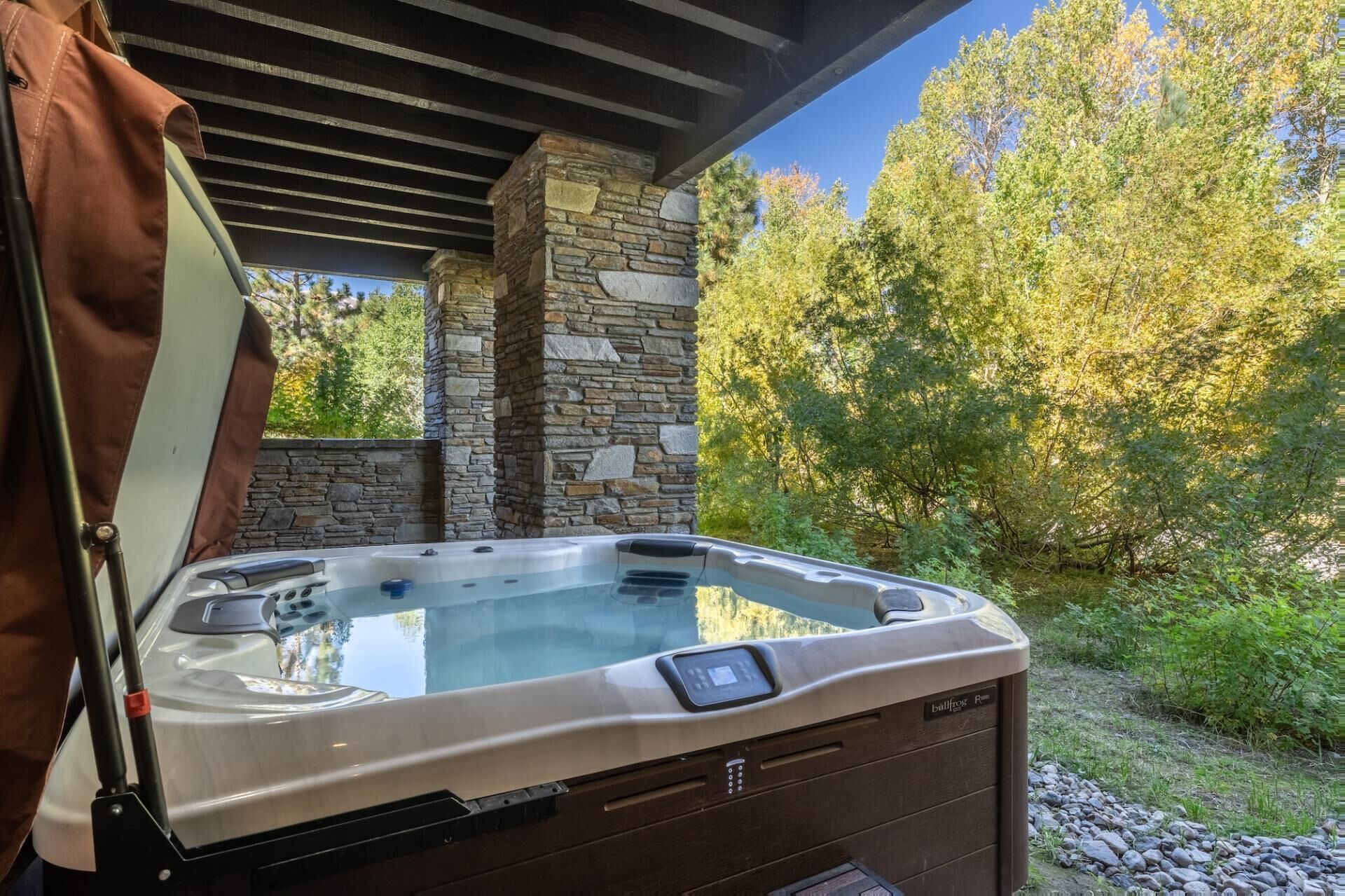 Ein Whirlpool unter einer Pergola mit Steinmauern und Blick auf einen Wald.