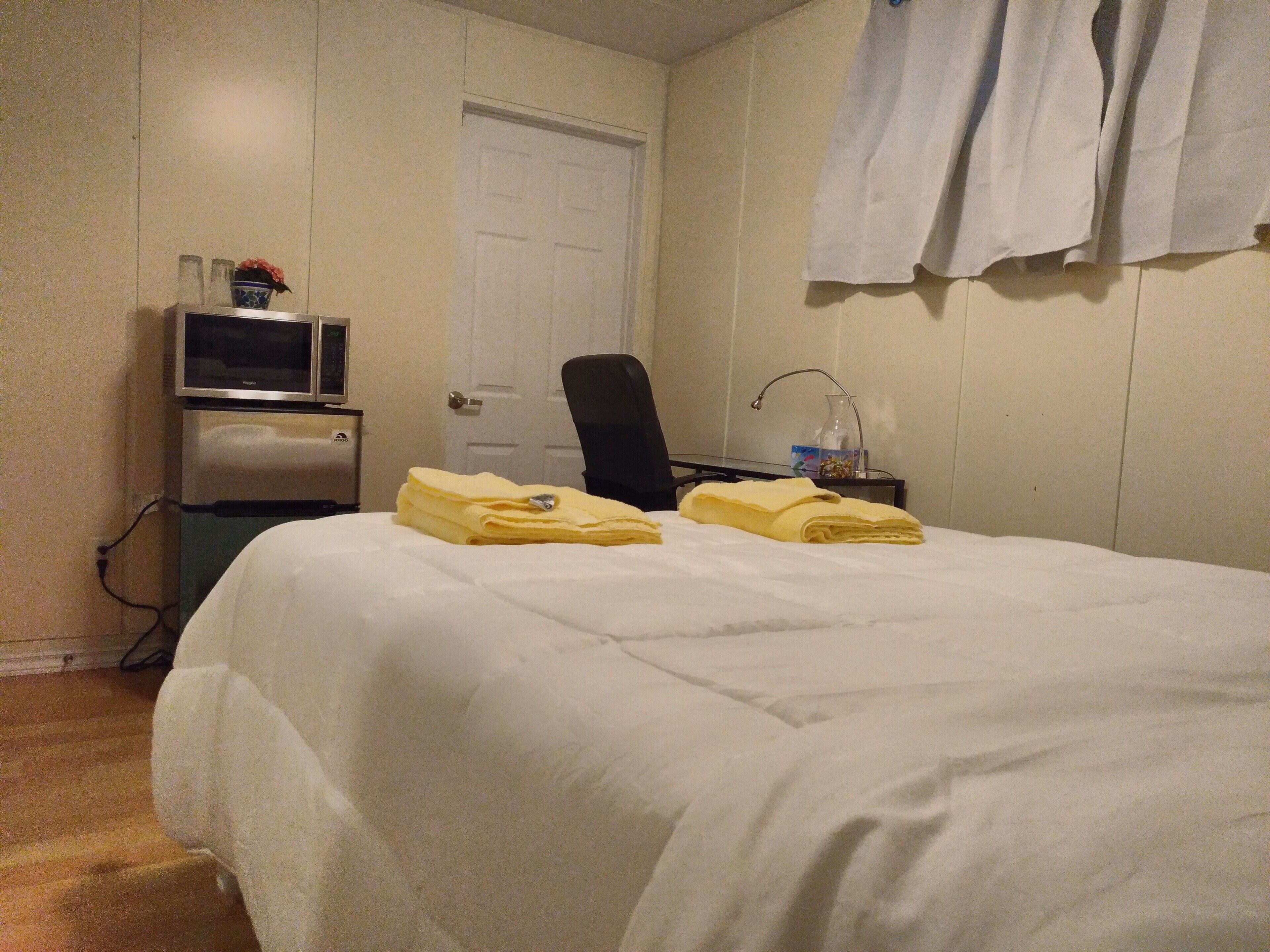 A hotel room with a bed, a desk, a chair, a television, and a door.
