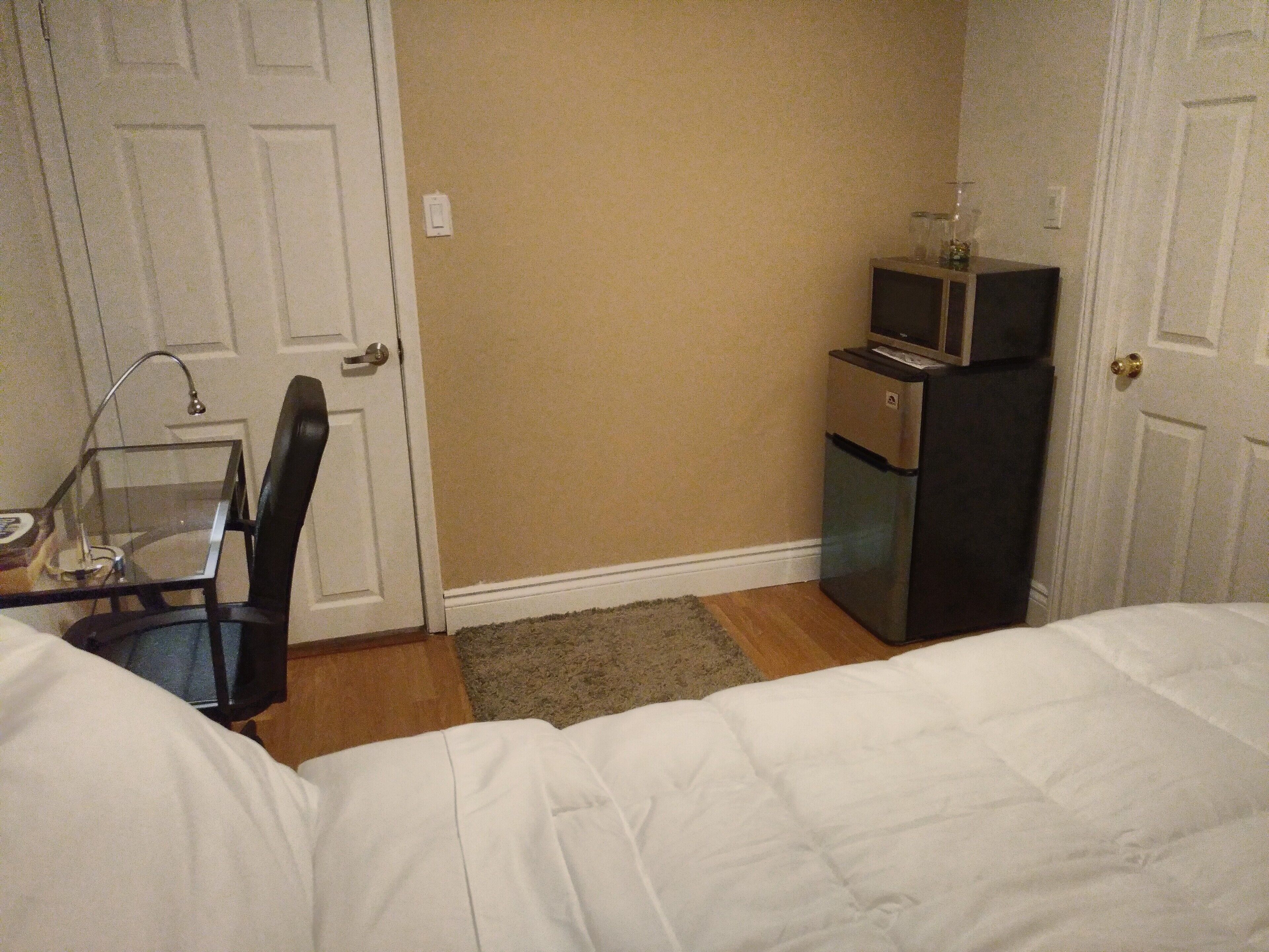 A small hotel room with a bed, a desk with a chair, a television, and a refrigerator.