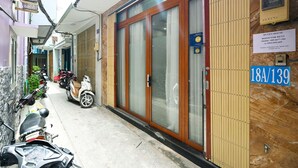 Une rue étroite bordée de scooters et de motos garés, un immeuble avec une grande porte vitrée et une enseigne indiquant le numéro de la pièce : 18A/139.
