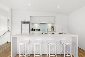 A modern kitchen with white cabinetry, a central island with bar stools, and a stainless steel sink.