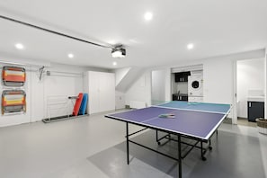 A ping pong table in a room with a ceiling-mounted projector, a washing machine, and a drying rack. - Surf Central (Lorne)