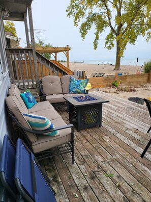 Une terrasse en bois aménagée avec du mobilier d’extérieur, notamment un canapé et des fauteuils, ainsi qu’un foyer.