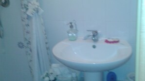 A bathroom with a white sink, a shower curtain, and a small shelf with toiletries. - BIJOUX HOUSE 3 DBLE BEDROOMS/2 SHOWERS+WC/FABBEACHES/ALL TRANSPORT LINKS (Miracoli)