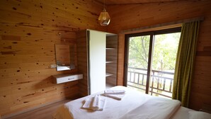 Ein Schlafzimmer einer Holzhütte mit einem Bett, einem Spiegel, einem Regal und einem Fenster mit Vorhängen.