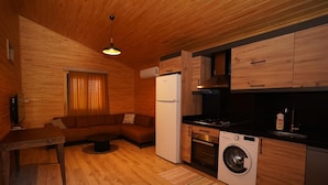 Ein kompakter Wohnbereich mit Sofa, Esstisch, Küchenzeile inklusive Herd, Backofen und Waschmaschine, sowie Holzwänden.