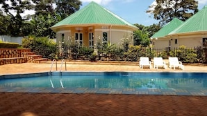 A swimming pool with lounge chairs, two green-roofed buildings, and a brick pathway. - Lyden Cottages (Kampala)