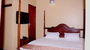 A neatly made bed with a wooden headboard, a bedside table with a telephone, and a television mounted on the wall. - Lyden Cottages (Kampala)