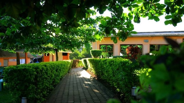 A pathway lined with neatly trimmed hedges and a building with a tiled roof in the background. - Lyden Cottages (Kampala)