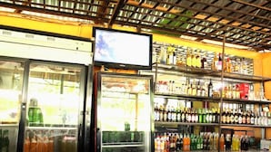 A bar area with a television mounted on the wall, shelves stocked with various bottles, and a refrigerator with beverages. - Lyden Cottages (Kampala)