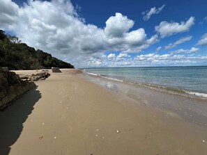 A beach with a stone wall, calm water, and a clear sky.