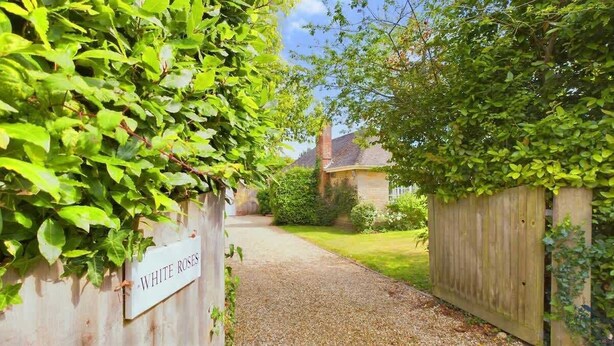 A gravel path leading to a house with a wooden fence and a sign indicating 'WHITE ROSES'. - White Roses a dog friendly retreat for two (Bembridge)