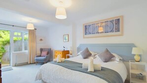 A bedroom with a large bed, a chair, a nightstand, and a window with curtains. - White Roses a dog friendly retreat for two (Bembridge)