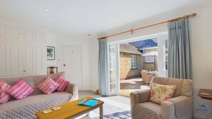 A living room with a sofa, armchair, and a table. There is a door leading to a balcony. - White Roses a dog friendly retreat for two (Bembridge)