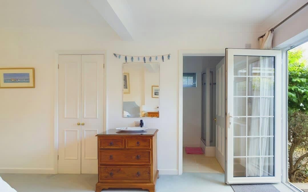 A room with a wooden dresser, a white door, a mirror, and a sliding glass door leading outside.