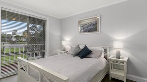 A bedroom with a large window, a bed with white bedding, two bedside tables with lamps, and a framed picture on the wall. - Settle Inn, Settlement Rd holiday house, close to shops and beach! (Cowes)