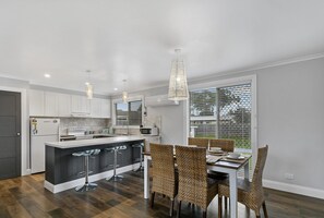A modern kitchen with white cabinets, a central island with bar stools, and a dining area with wicker chairs.