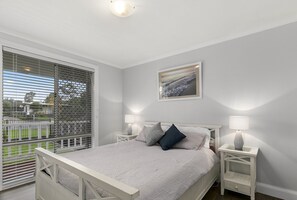 A bedroom with a large window, a bed with white bedding, two bedside tables with lamps, and a framed picture on the wall.