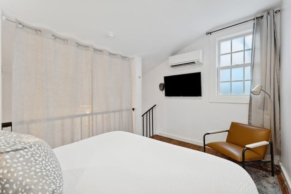 A hotel room with a bed, a chair, a TV, and an air conditioning unit. - Exclusive Open Loft in Downtown Charleston (Charleston)