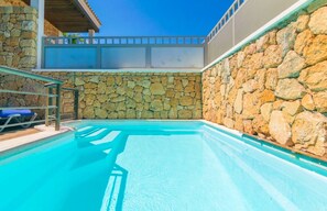 Relax by the pool surrounded by a serene atmosphere and a stone wall.