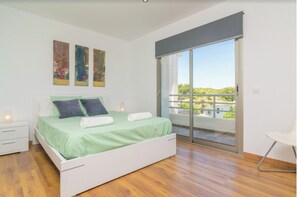 Relax in this serene bedroom with a single bed, nightstand, and chair, offering a peaceful view of lush greenery from the balcony.