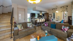 A modern living room with a staircase, a kitchen in the background, and a dining area. - Protaras Villa Rocco Near The Beach (Protaras)