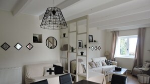 Un salon moderne avec une table à manger, des canapés blancs et une grande fenêtre agrémentée de rideaux.