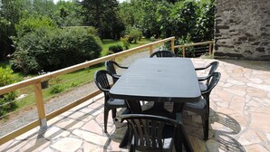 Une terrasse extérieure avec une table et des chaises en pierre, donnant sur un jardin où poussent différentes plantes et arbres.