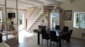 Un vaste espace de vie agrémenté d’un escalier en bois, d’une table à manger avec des chaises et d’un téléviseur fixé au mur.