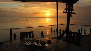 Vista al atardecer desde un restaurante frente a la playa, con mesas y sillas, con vista al océano.