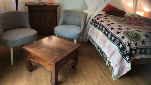 Un dormitorio acogedor con cama, dos sillones, una mesa de madera, una mesita de noche, una lámpara y una planta en maceta.