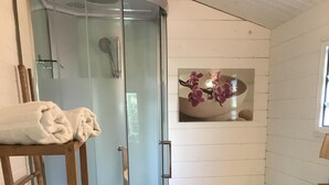 Un baño con cabina de ducha de vidrio, inodoro, lavabo y repisa con toallas.