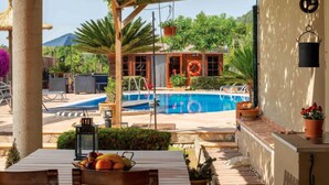 A pool area with a view of a house, a table with fruit, and a hanging lantern. - Private Villa with AC, Wifi, huge pool, garden, sun terraces and BBQ, in Selva (Selva)
