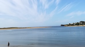 A beach with a person walking along the shore, calm water, and a clear sky with clouds. - PORT CROUESTY apartment with pool (Arzon)