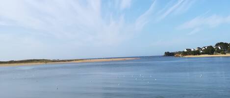 A beach with a person walking along the shore, calm water, and a clear sky with clouds.