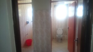 A bathroom with a toilet, a red bucket, and tiled walls.