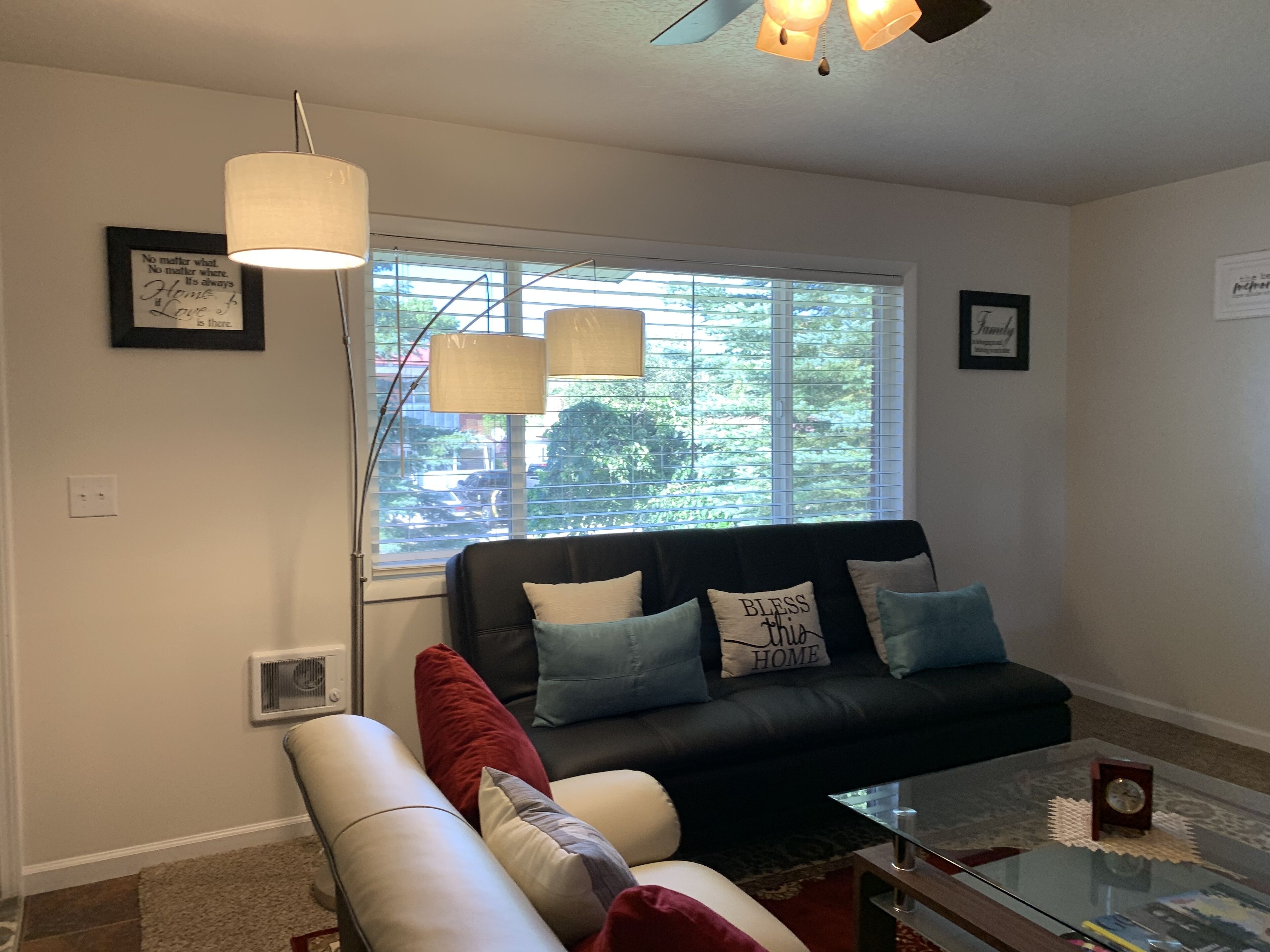 A living room with a black leather sofa, a glass coffee table, and a window with blinds.