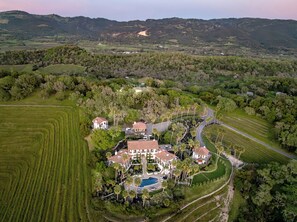 An aerial view of a large estate with multiple houses, a swimming pool, and surrounding green fields.